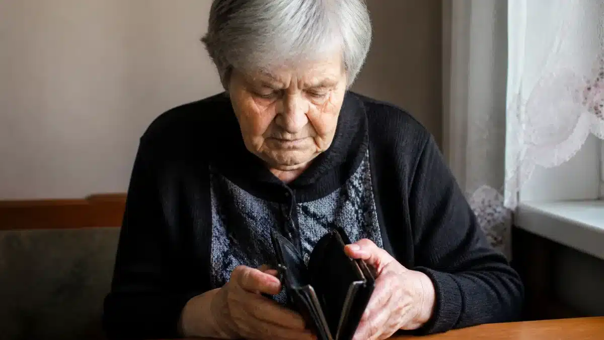 Personne agee assise seule, tete baissee, portefeuille vide dans les mains