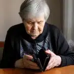 Personne agee assise seule, tete baissee, portefeuille vide dans les mains
