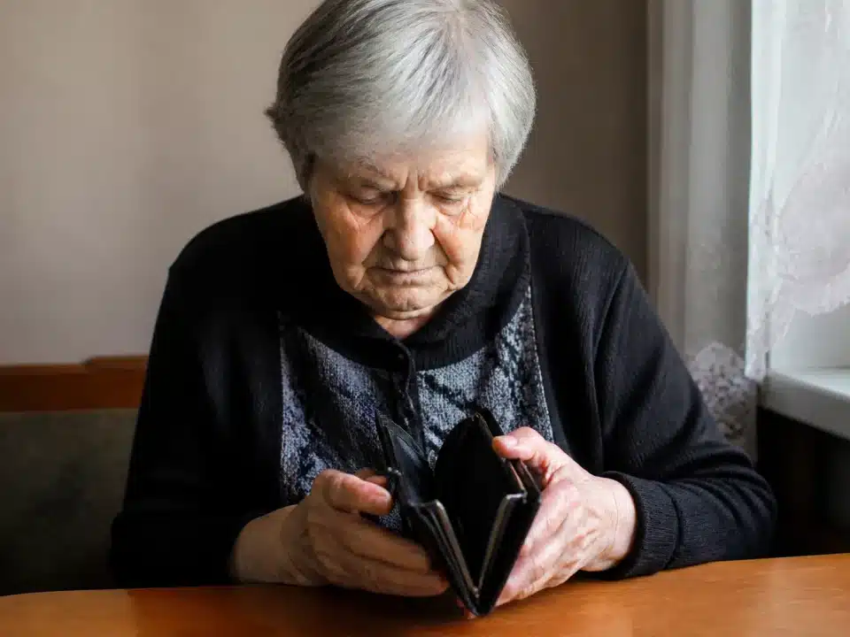 Personne agee assise seule, tete baissee, portefeuille vide dans les mains