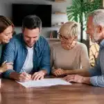 Parents et enfants adultes assis autour table signant documents immobiliers