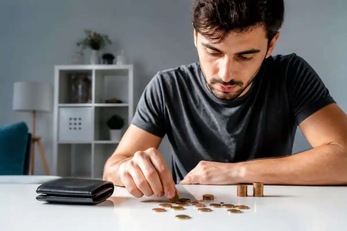 Homme jeune comptant des pieces de monnaie sur table blanche