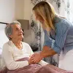 Personne agee assise recevant visite famille membre debout pres lit
