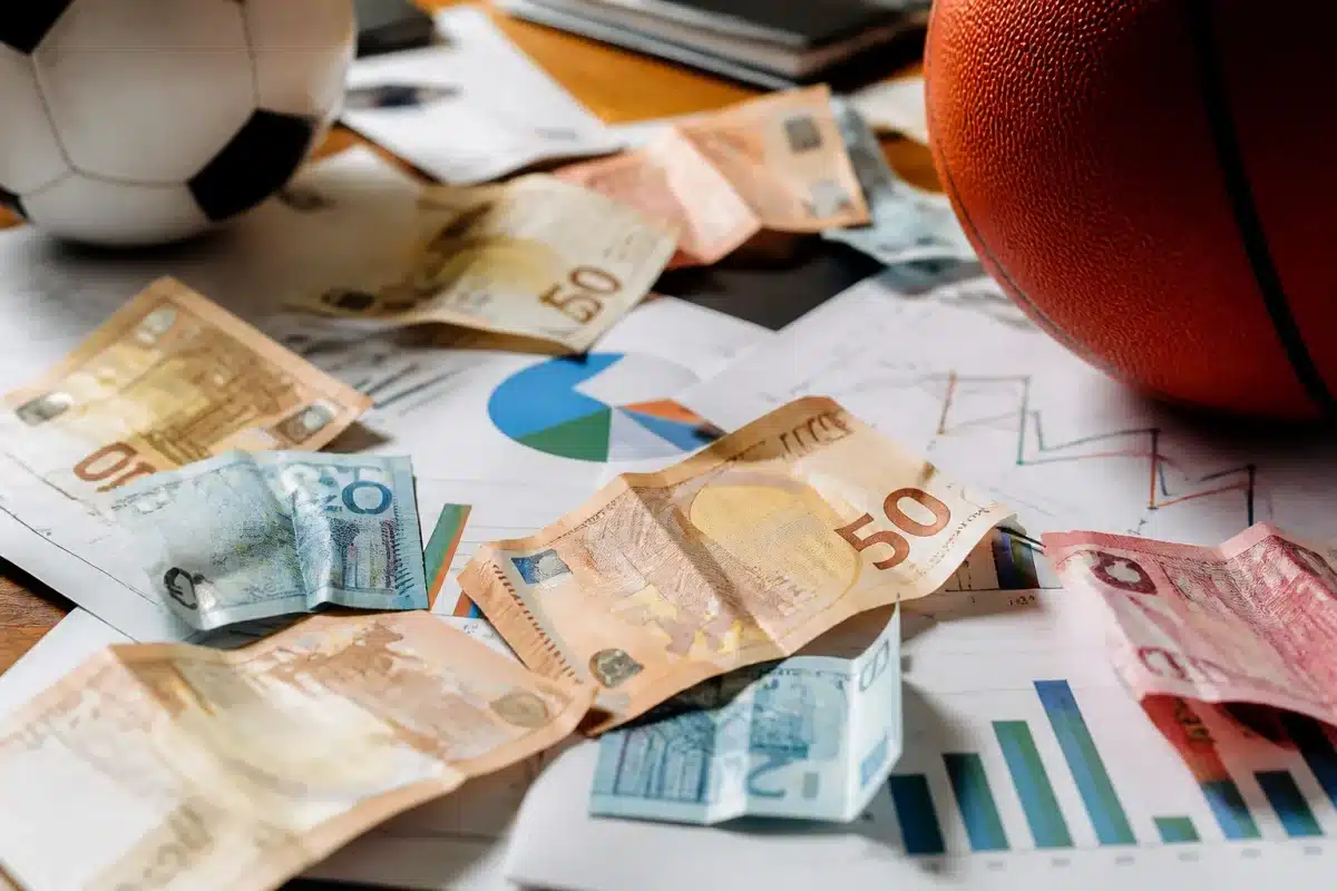 Billets dispersés sur documents sportifs variés montrant fragmentations budgetaires