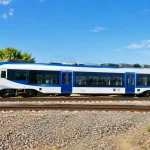 Train blanc et bleu stationnant sur rails, vue de côté complète