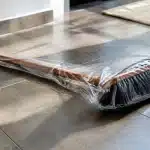 Balai enveloppé d'un sac plastique transparent, posé horizontalement sur sol.