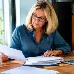 Femme age assise a bureau verifiant documents retraite papiers