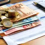 Billets et pieces de monnaie empiles sur document officiel 2026