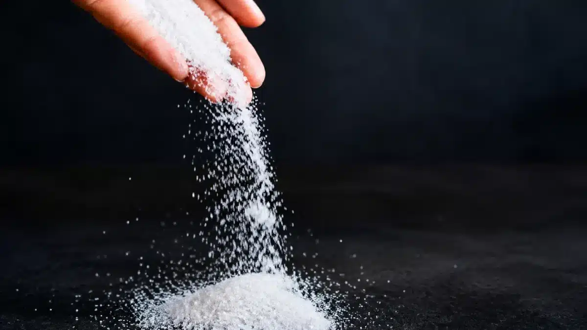 Poudre blanche granuleuse versée d'une main sur surface sombre