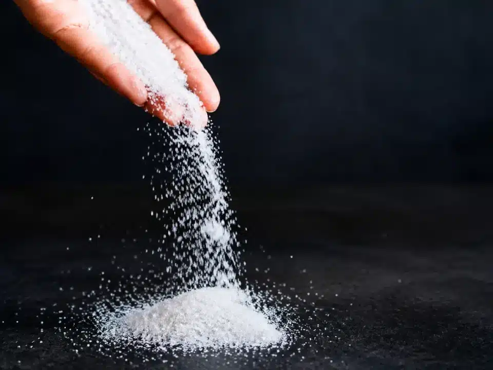 Poudre blanche granuleuse versée d'une main sur surface sombre