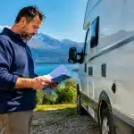 Homme tenant documents pres camping-car stationnaire inspectant details