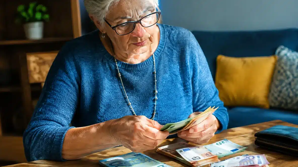 Personne agee assise comptant des billets d'euros sur table