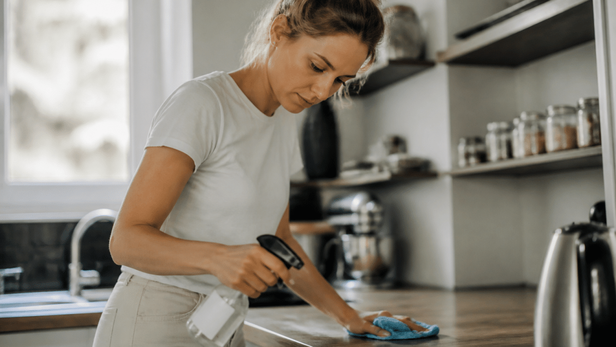 Femme nettoyant comptoir cuisine avec produit spray et chiffon
