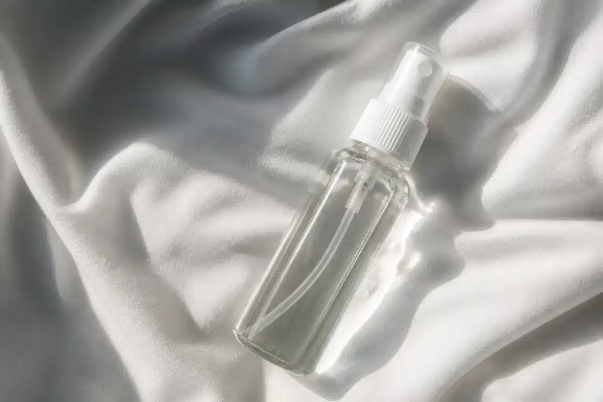 Flacon pulverisateur rempli de liquide clair sur tissu blanc.